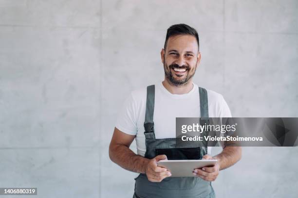 jeune travailleur masculin en uniforme général utilisant une tablette sur son lieu de travail. - salopette photos et images de collection
