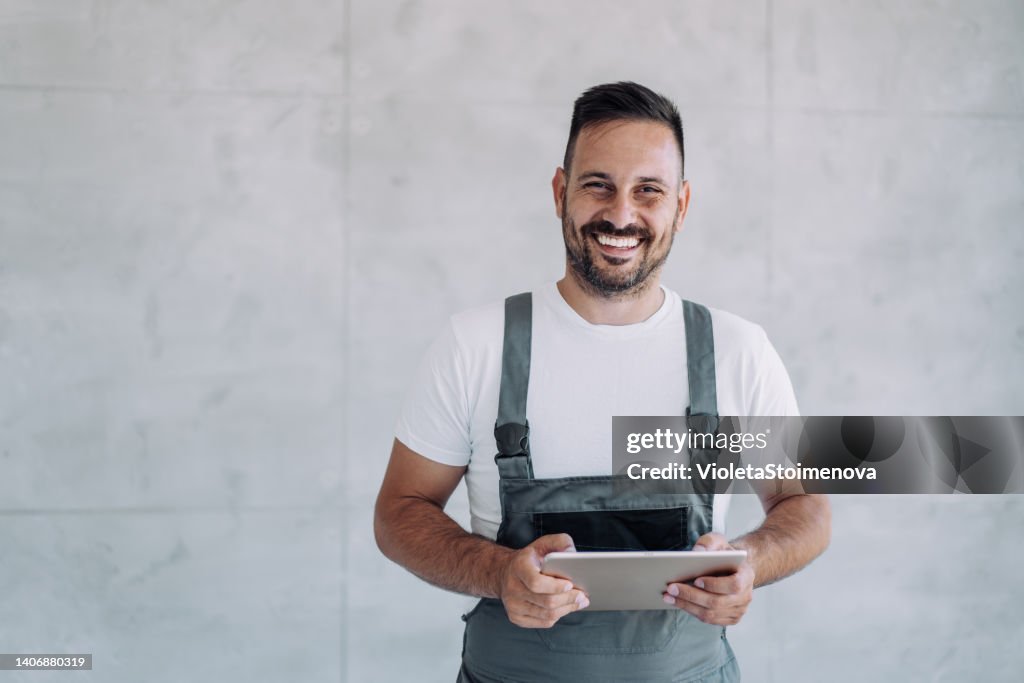 Young male worker in an overall uniform using tablet at his workplace.