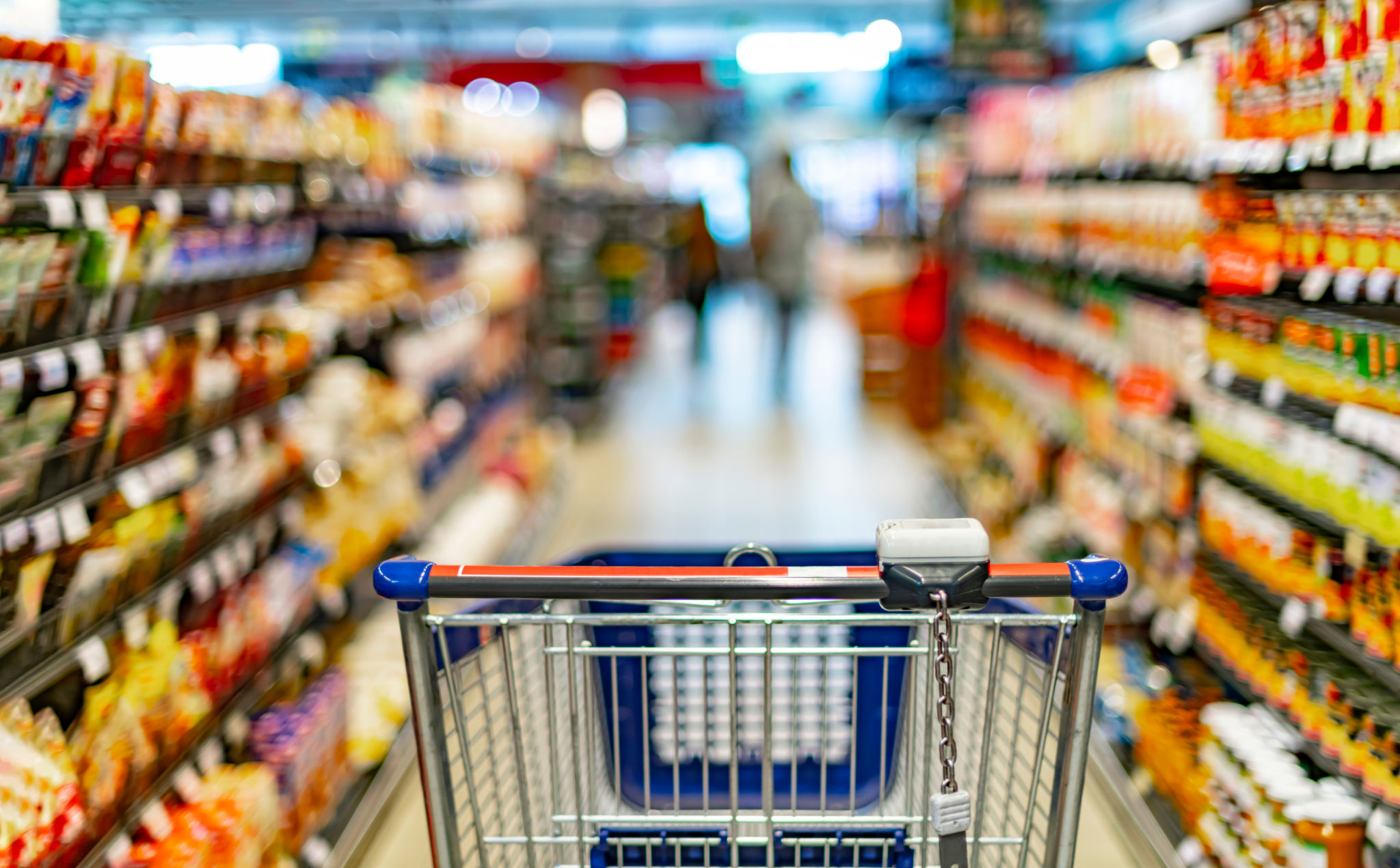 A shopping cart by a store shelf in a supermarket A shopping cart by a store shelf in a supermarket