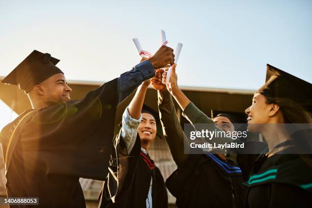 eine gruppe fröhlicher menschen bei der graduierung, die gemeinsam diplome oder zertifikate hochhalten und erfolge feiern. diverse multiethnische junge studenten in schwarzen gewändern außerhalb der universitätshochschule - university building stock-fotos und bilder