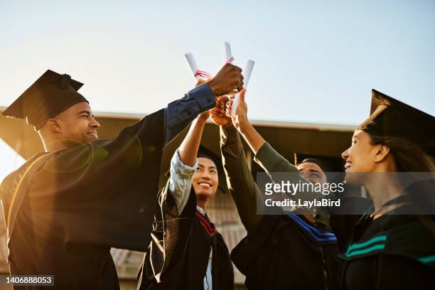 a group of cheerful people at graduation, holding diplomas or certificates up together and celebrating success. diverse multiethnic young students in black robes outside university college institution - masters degree imagens e fotografias de stock