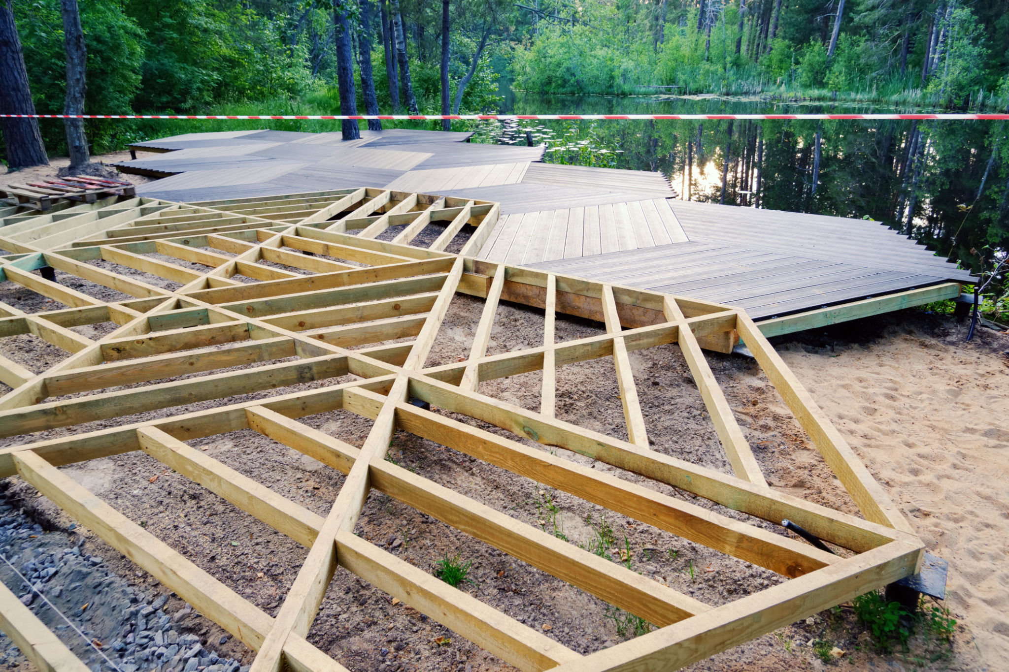 Walking area on screw piles, wooden frame, plastic terrace board on pond shore in park, construction site Walking area on screw piles, wooden frame, plastic terrace board on pond shore in park, construction site