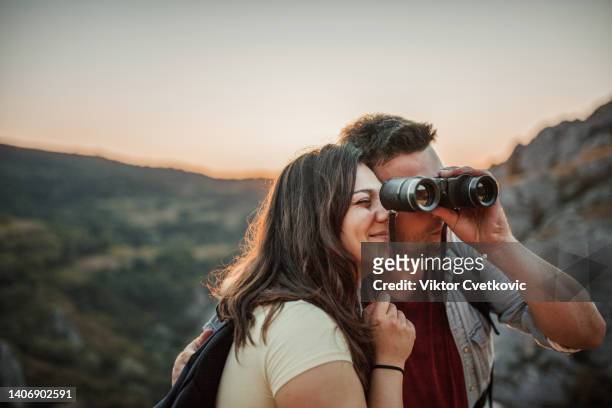 happy couple with backpacks bird watching and looking at the view from mountain - bird watching stock pictures, royalty-free photos & images