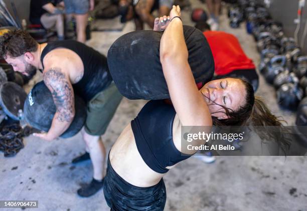Alexa Hoovis throws a sandbag over her shoulder during a workout at the Strength Factory gym on July 4, 2022 in Baldwin, New York. The athletes use...