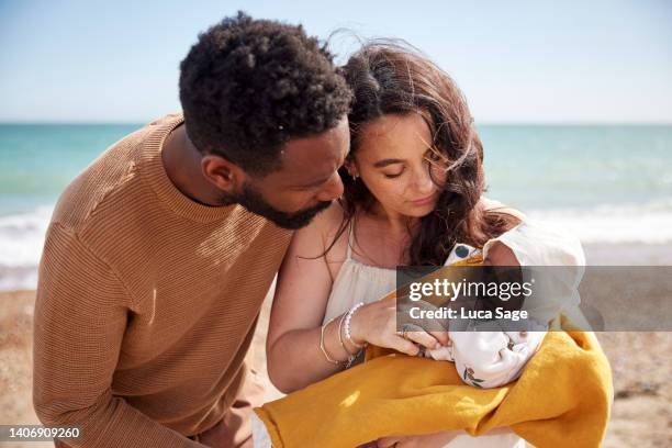 mother and father, looking adoringly at their newly born baby daughter, on the beach enjoying her first trip to the coast. - lebensversicherung stock-fotos und bilder