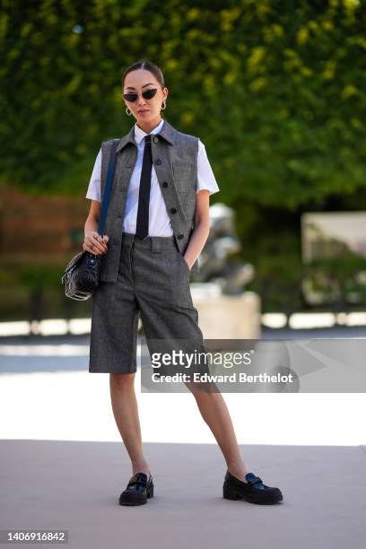 Chriselle Lim wears black cat eyes sunglasses, silver earrings, a white short sleeves shirt, a black tie, a gray sleeveless / buttoned gilet from...