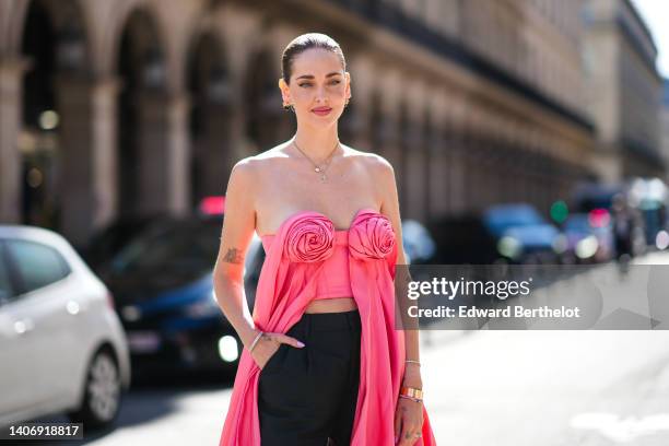 Chiara Ferragni wears black sunglasses, gold earrings, a gold chain pendant necklace, a pink shiny satin square-neck / shoulder-off / flower pattern...