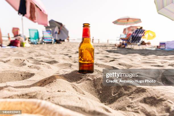 cold beer leaning on the sand of a beach. sea and people in the background. - incidental people stock pictures, royalty-free photos & images