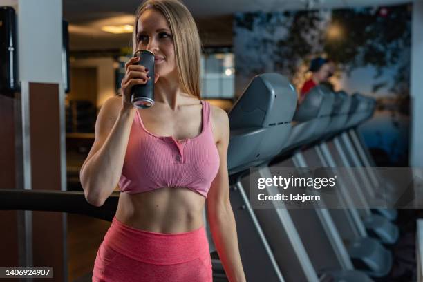 frau mit einem energy-drink steht im fitnessstudio - energydrink stock-fotos und bilder
