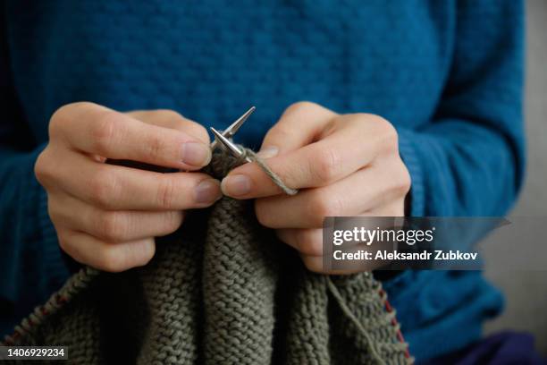 the girl is holding knitting and metal knitting needles in close-up. a freelance woman knits a wool sweater or clothes at home. the concept of hobbies, creativity, needlework, handmade. do what you love. home life, a break from household chores. - elastisch weefsel stockfoto's en -beelden