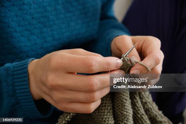 the girl is holding knitting and metal knitting needles in close-up. a freelance woman knits a wool sweater or clothes at home. the concept of hobbies, creativity, needlework, handmade. do what you love. home life, a break from household chores. - elastisch weefsel stockfoto's en -beelden