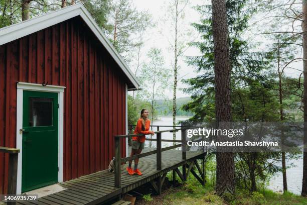 female meets the scenic summer morning at the red cabin by lakeshore in sweden - cabin stock pictures, royalty-free photos & images