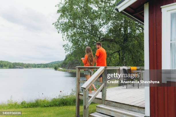 female and male contemplating summer morning drinking coffee by the red cabin with lake view in sweden - north bildbanksfoton och bilder