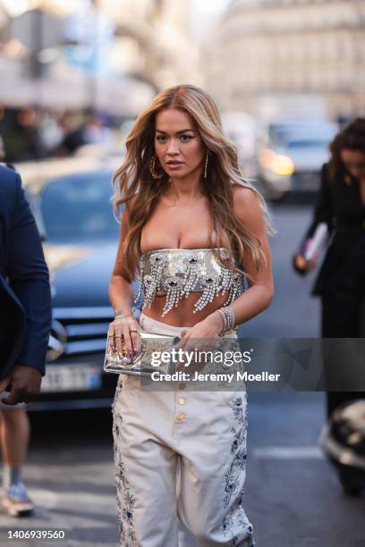 Rita Ora seen wearing a silver rhinestones off-shoulder bralette, gold earrings and a creme white flower embroidered denim jeans, outside the...