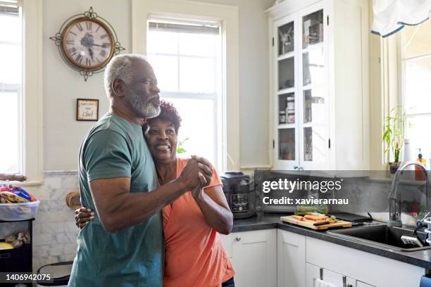 playful black seniors embracing and dancing in kitchen - couple dancing at home stockfoto's en -beelden