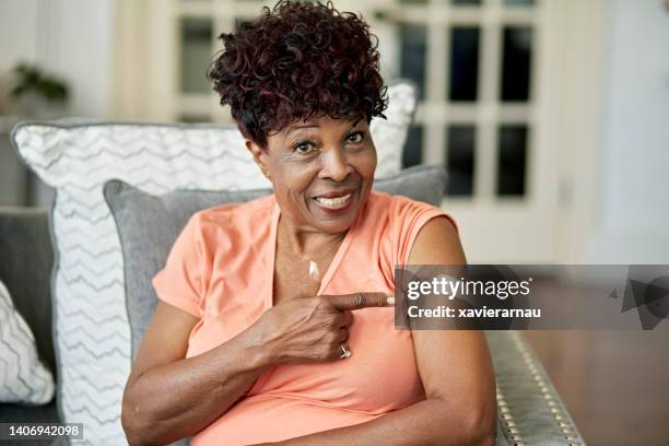 black woman in late 70s pointing to vaccination - covid vaccine bandage stock pictures, royalty-free photos & images