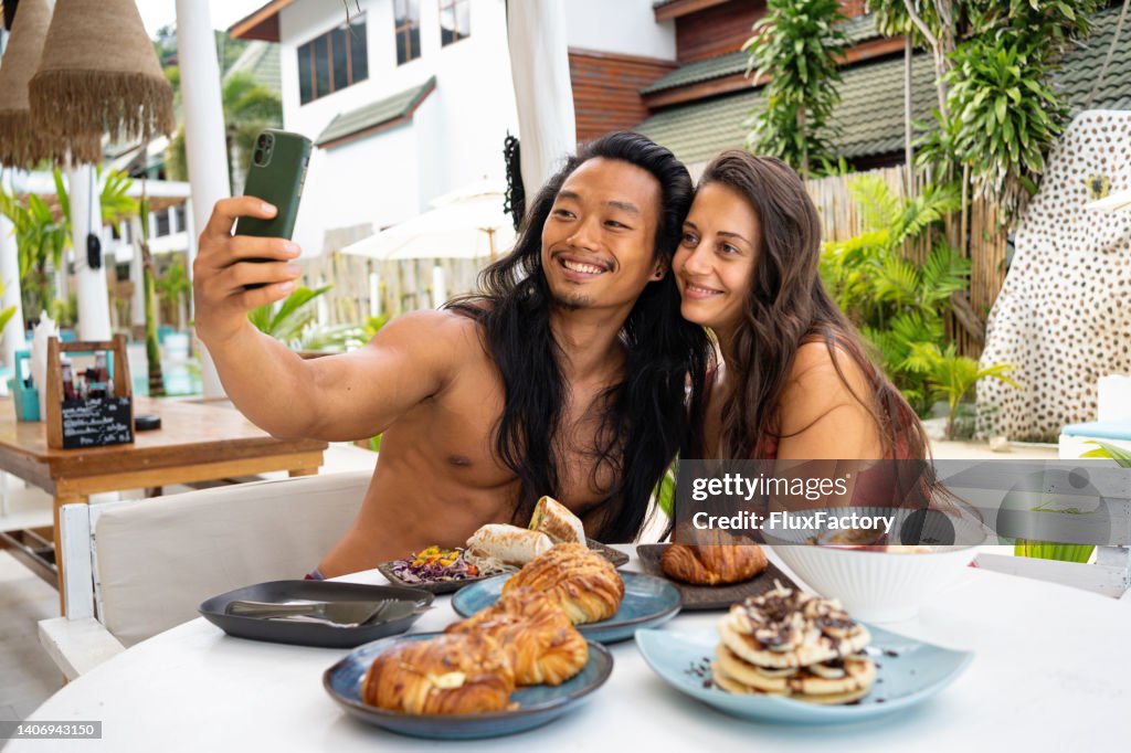 Multiracial couple taking selfie, during breakfast at the beach restaurant