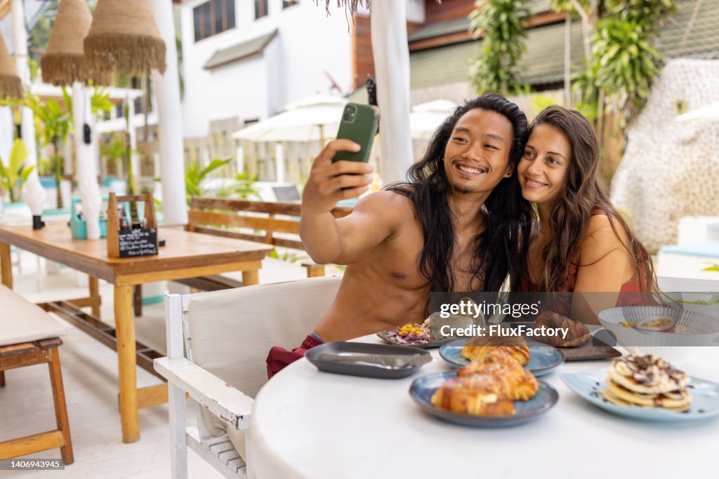 Multiracial couple taking selfie, during breakfast at the beach restaurant