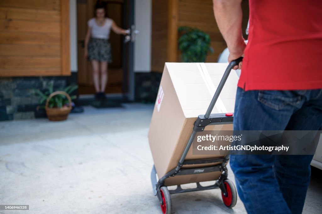 Unrecognizable delivery guy delivering prcels with cart to womans front door.
