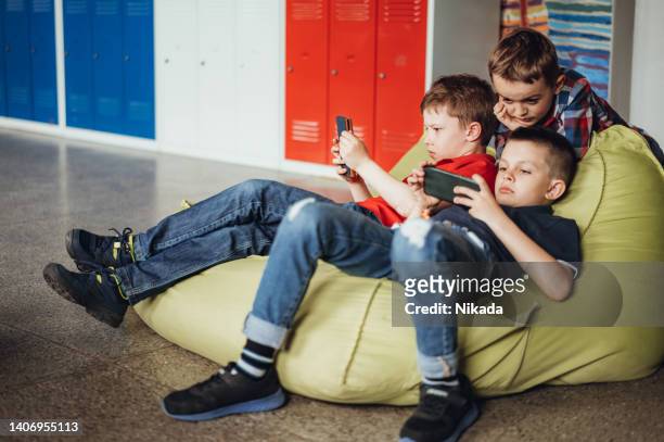 male friends playing games on smart phones while taking break in school - game three stockfoto's en -beelden