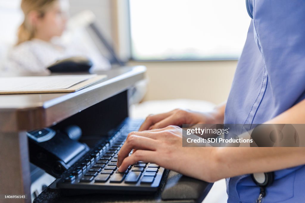 Focus on healthcare worker's hands typing on computer keyboard
