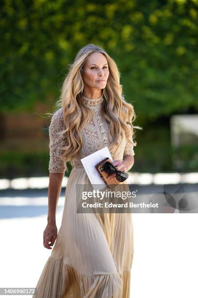 Elle Macpherson wears a beige lace pattern high neck / long sleeves body, a matching beige pleated midi skirt, black sunglasses, outside the Dior...