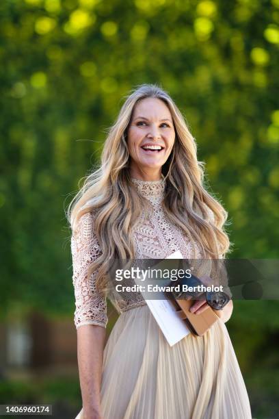 Elle Macpherson wears a beige lace pattern high neck / long sleeves body, a matching beige pleated midi skirt, black sunglasses, outside the Dior...