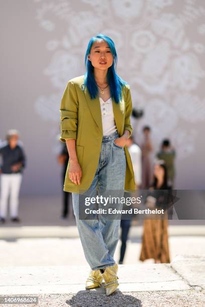 Margaret Zhang wears gold chain necklace, a white ribbed / buttoned neck t-shirt, a green oversized blazer jacket, blue denim large pants, yellow...