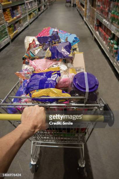 pov of man pushing a full trolley down a supermarket aisle - einkaufswagen voll stock-fotos und bilder