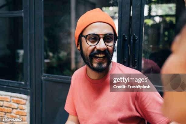 un apuesto joven hipster feliz riendo mientras habla con su irreconocible novia - fond orange fotografías e imágenes de stock