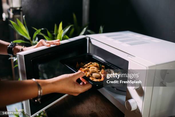 ein beschnittenes foto einer anonymen kaukasischen frau, die essen im ofen erhitzt - asiatisch kochen stock-fotos und bilder