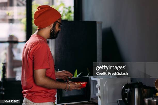 a serious man standing in the kitchen and heating food in the oven - microwave oven stock pictures, royalty-free photos & images