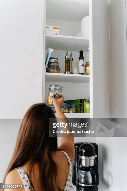 woman storing a glass container in her kitchen cabinet - dispensa foto e immagini stock
