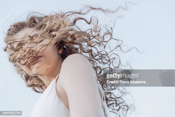 beautiful woman with long curly hair standing against the wind - hair styling photos et images de collection