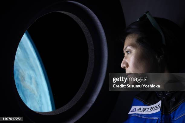 a commercial space traveler looking at the earth throughout  the window at inside of the spaceship. - astronaut stock-fotos und bilder