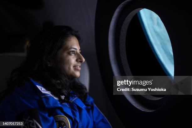 A commercial space traveler looking at the earth throughout  the window at inside of the spaceship.