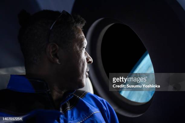 A commercial space traveler looking at the earth throughout  the window at inside of the spaceship.