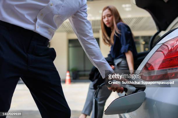 asian businessman and business woman putting charger for his electric car. sustainable and renewable energy concept - electric car charger imagens e fotografias de stock