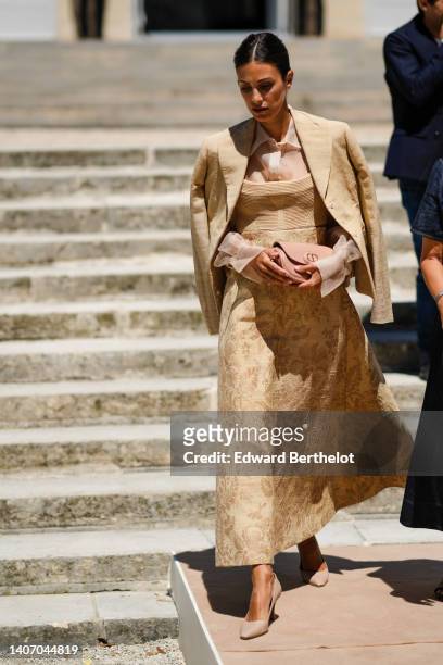 Alessandra de Osma wears a beige silk shirt, a beige ribbed shoulder-off top / flower print pattern long dress from Dior, a beige blazer jacket, a...