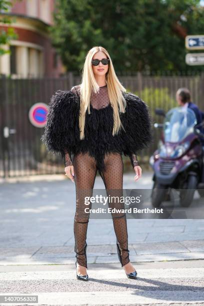 Chiara Ferragni wears black sunglasses from Ray Ban, a black polka dots print pattern long sleeves jumpsuit, a black oversized feathers / fluffy /...