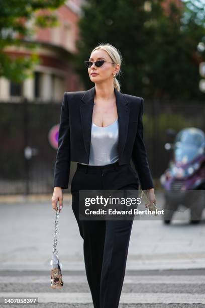 Justyna Czerniak wears black cat eyes sunglasses, silver earrings, a silver shiny V-neck body, a black blazer jacket with epaulets, black large suit...