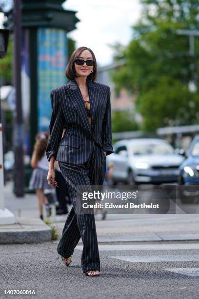 Chriselle Lim wears black sunglasses, a black bra underwear, a black with striped print pattern oversized blazer jacket, matching black striped print...