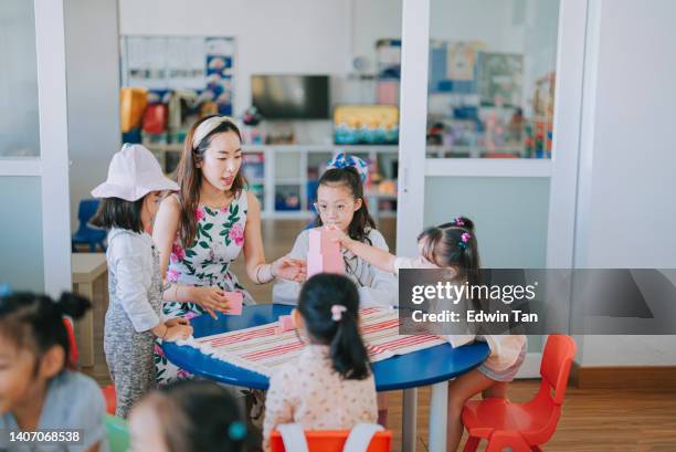 アジア系中国人モンテッソーリ幼稚園の女子教師が、教室のおもちゃのブロックのある建物の塔に生徒を見せる - surrounding ストックフォトと画像