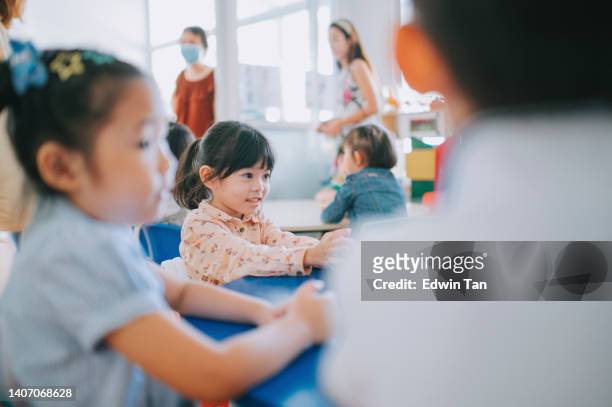 aufgeregtes asiatisch-chinesisches montessori-vorschulmädchen, das mit ihrer klassenkameradin am ersten schultag im klassenzimmer sitzt - montessori education stock-fotos und bilder
