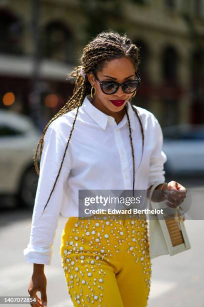 Ellie Delphine wears black sunglasses, gold earrings, a gold necklace, a white shirt, a gold Juste Un Clou bracelet from Cartier, gold rings, a white...
