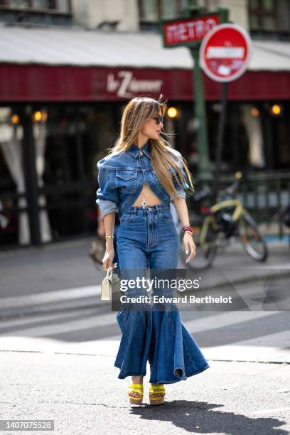 Heart Evangelista wears black sunglasses, a blue denim asymmetric cropped shirt, blue denim matching ruffled flared pants, burgundy pearls bracelets,...