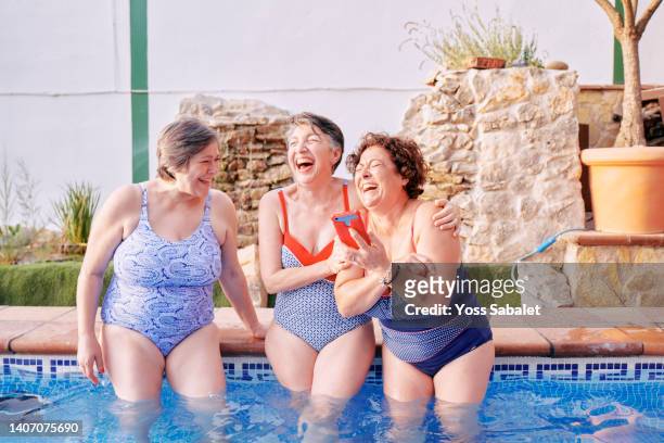 group of mature female friends having fun at the pool with a phone - voluptuous stock pictures, royalty-free photos & images
