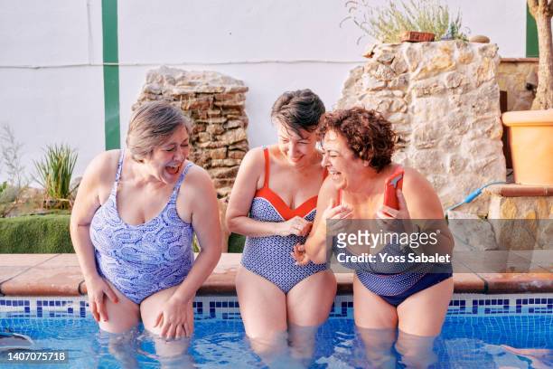mature female friends having fun in the pool with a mobile phone - voluptuous stock pictures, royalty-free photos & images