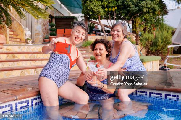 adult women at the pool drinking cocktails and taking a selfie - middle aged woman bathing suit stock pictures, royalty-free photos & images