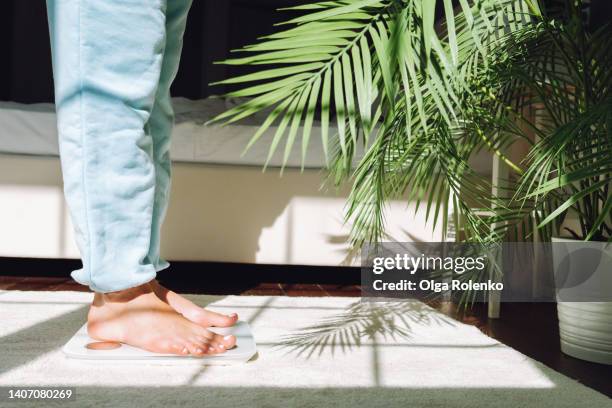 cropped woman legs standing on white weighting scales at home, checking her health - weigh in stock-fotos und bilder